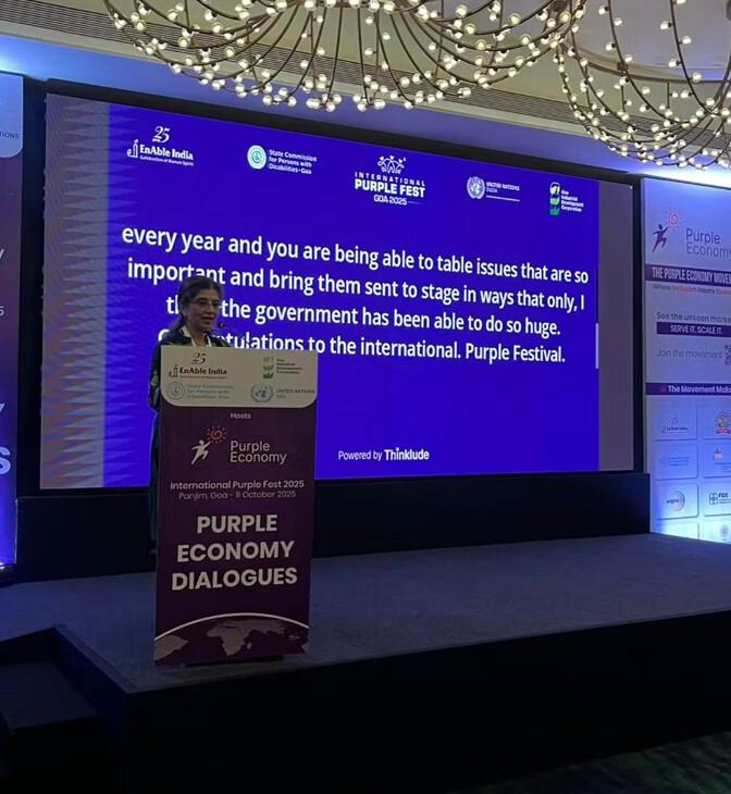 Thinklude live captions in English on the main screen at International Purple Fest 2025 in Goa, while a speaker addresses the room.